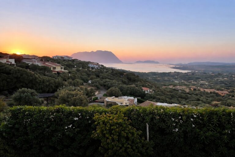 Sunset view over the hills around Olbia with scattered homes, Mediterranean vegetation, and the Gulf of Olbia stretching toward distant mountains.
