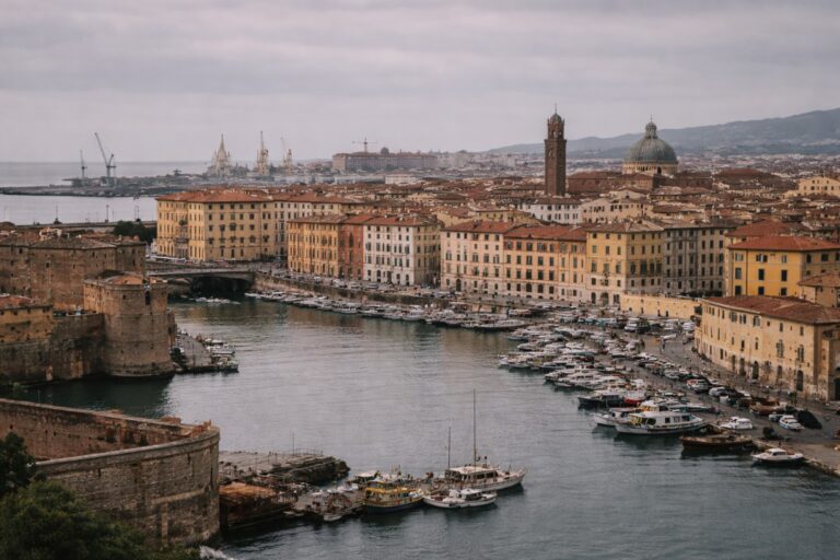 Livorno harbor with canal, small boats, port cranes and coastal skyline under muted light.