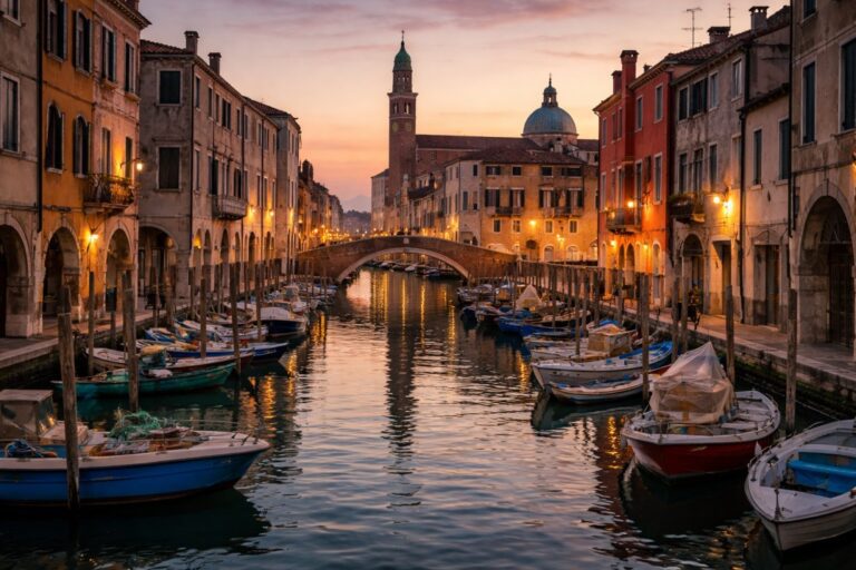 Canal in Chioggia at sunset with fishing boats, stone bridge and the bell tower along Corso del Popolo.