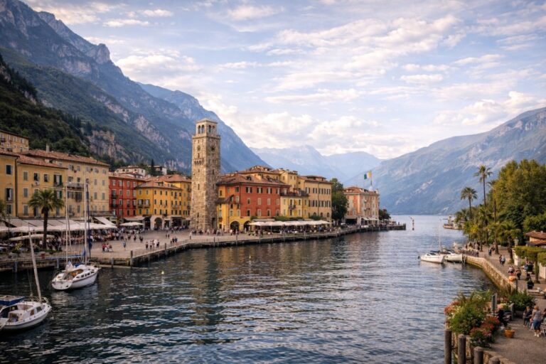 Riva del Garda harbor with Torre Apponale and colorful buildings on the northern shore of Lake Garda surrounded by mountains.