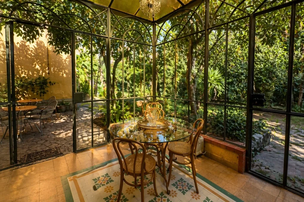 Glass conservatory dining space at Beet Community Botanical Garden coliving in Palermo, Sicily