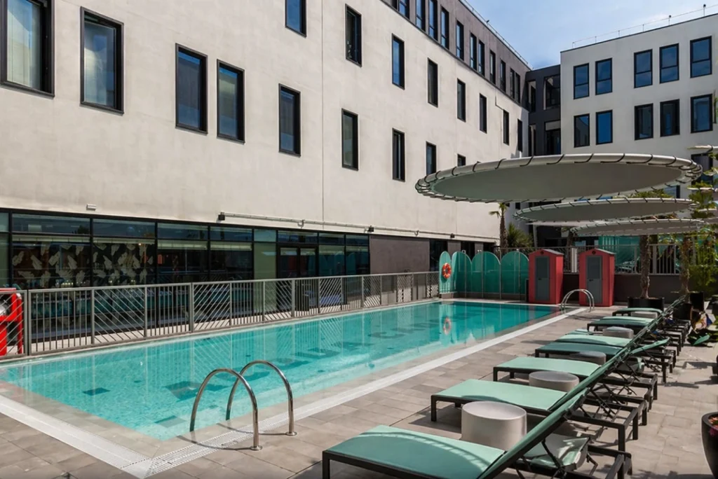 Outdoor pool courtyard at The Social Hub Bologna with sun loungers and modern coliving building